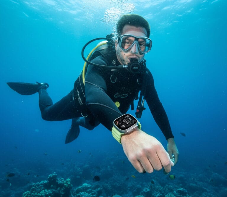 غواص يرتدي ساعة Apple Watch Ultra 3 بسوار رياضي أخضر تحت الماء، يوضح مقاومتها للماء والضغط.